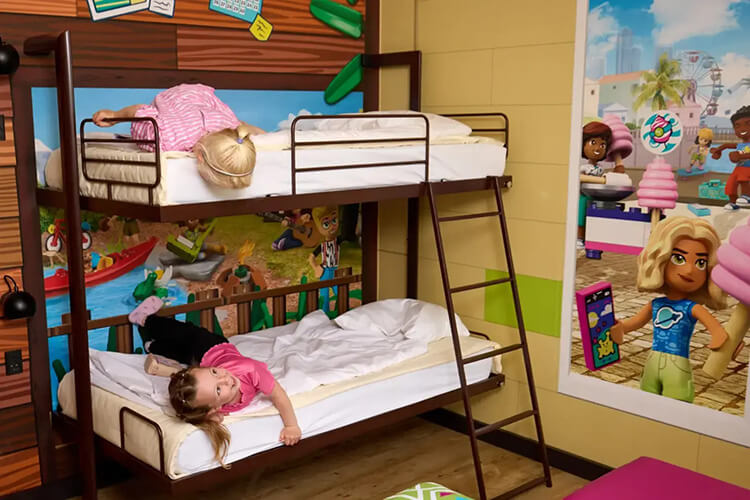 Zimmer mit Etagenbett, zwei Kindern darauf, bunte Wanddekoration mit Spielfigurenmotiven.