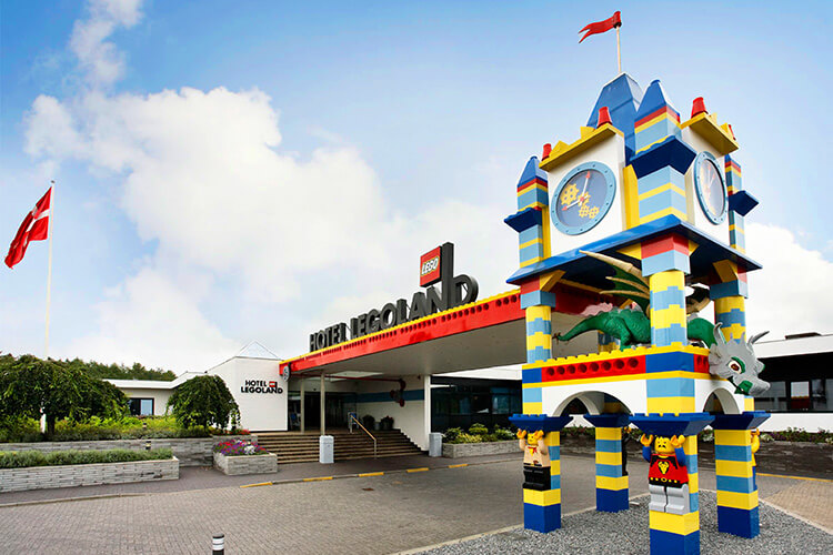 Eingangsbereich des Hotels LEGOLAND mit einer bunten, turmförmigen LEGO-Uhr und einer dänischen Flagge im Hintergrund.