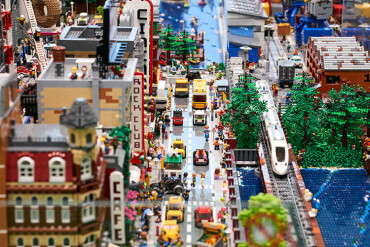 Miniaturstadt aus Lego mit Straßen, Fahrzeugen, Gebäuden, Bäumen und einem Zug auf Schienen.