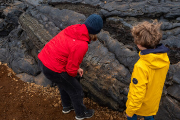 Zwei Kinder in roter und gelber Jacke betrachten Lavagestein.