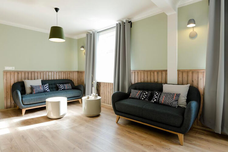 Wohnzimmer mit zwei dunkelgrauen Sofas, hellen Holzwänden, hellen Vorhängen und zwei runden Beistelltischen.