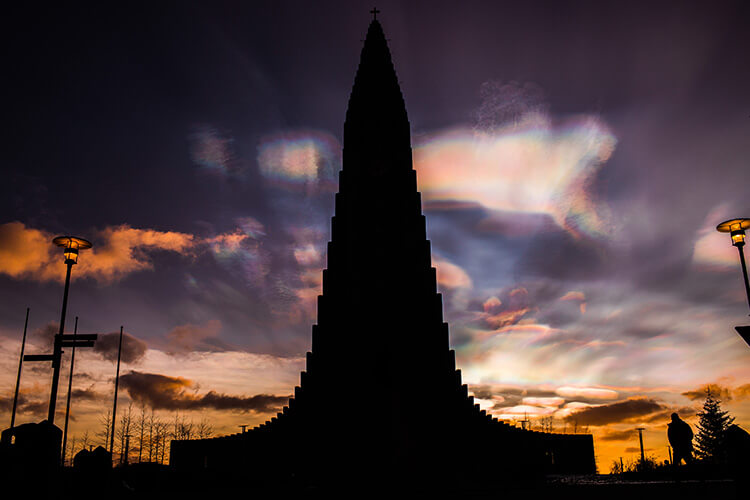 Silhouette der Hallgrímskirkja vor einem dramatischen Abendhimmel mit Wolken und zwei Straßenlaternen.