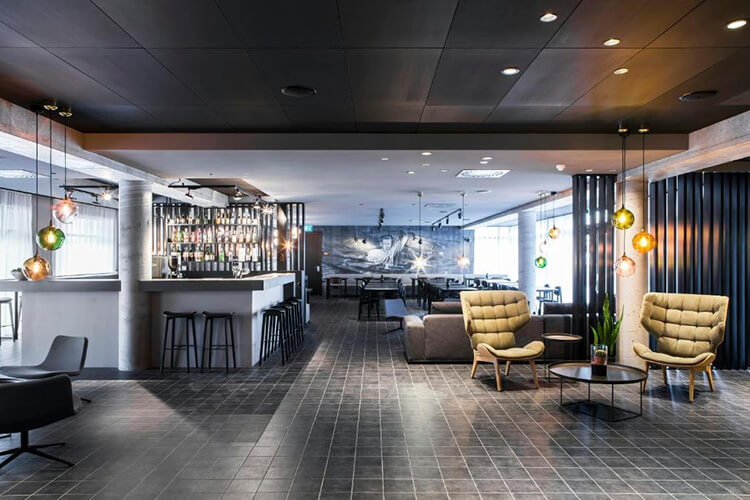 Moderne Hotellobby mit Bar, zwei gepolsterten Sesseln, Sofas und großem Wandbild im Hintergrund.