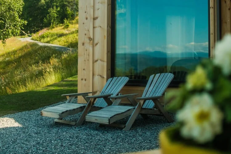 Zwei Liegestühle aus Holz stehen vor einem Holzhaus mit einer großen Fensterfront.