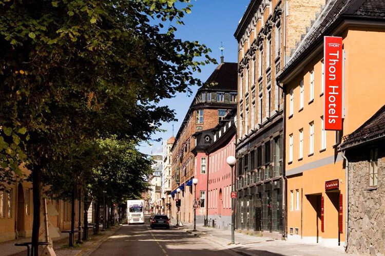 Eine Straße in Oslo mit Bäumen und Gebäuden. Man sieht den Eingang zu einem Hotel.