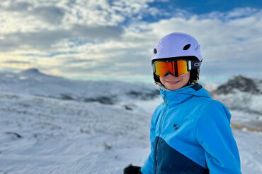 Kind mit Skihelm und Skibrille in blauer Winterjacke vor verschneiter Berglandschaft in Norwegen