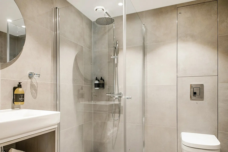 Modernes Badezimmer mit rundem Spiegel, Waschbecken, Glasdusche mit Regenduschkopf und Toilette