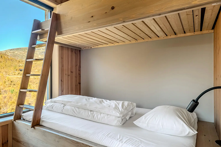 Holzhochbett mit weißer Bettwäsche und Leselampe vor Fenster mit Blick auf norwegische Landschaft