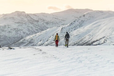 Zwei Personen mit Rucksäcken wandern im verschneiten norwegischen Gebirge bei Sonnenuntergang