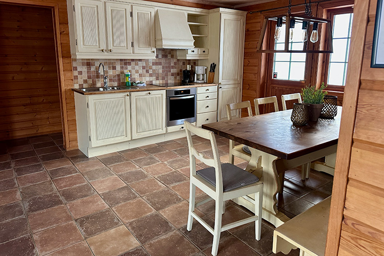 Rustikale Küche mit weißen Schränken, braunem Fliesenboden, Holztisch mit Stühlen und Holzverkleidung an den Wänden