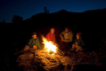 Eine Familie sitzt im Dunkeln um ein Lagerfeuer herum.