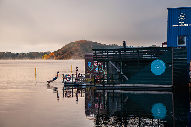 Eine schwimmende Sauna auf dem Oslofjord. Eine Person springt kopfüber ins Wasser. 