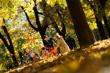 Eine Familie steht in einem Park und schmeißt buntes Herbstlaub in die Luft.