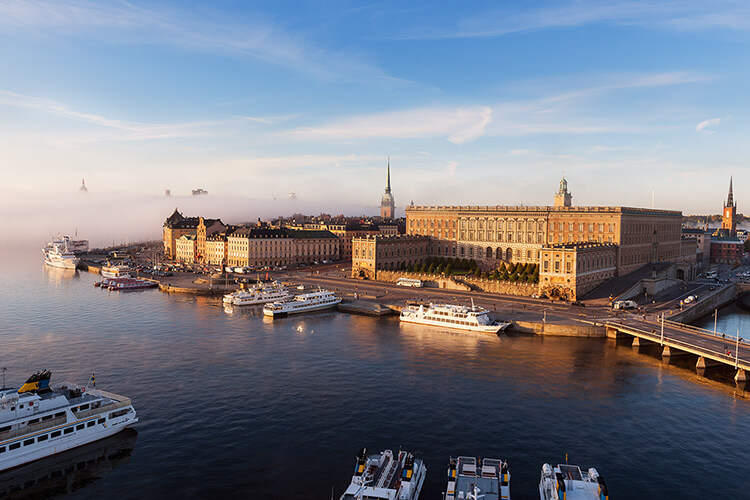 Blick auf die Altstadt von Stockholm mit historischen Gebäuden, mehreren angelegten Passagierschiffen und einer Brücke über das Wasser bei klarem Himmel