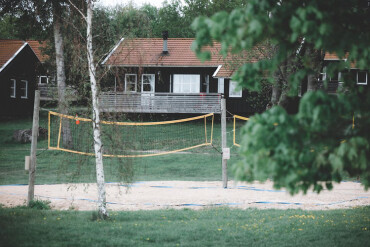 Sandvolleyballfeld mit Netz vor einem Holzhaus mit Terrasse und roten Dächern