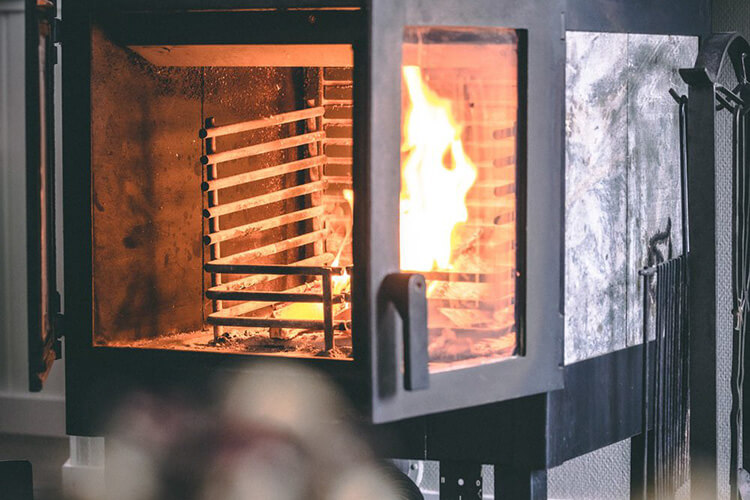 Brennender Kaminofen mit sichtbarem Feuer hinter Glastür und Metallgitter im Inneren