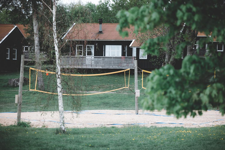 Sandvolleyballfeld mit Netz vor einem Holzhaus mit Terrasse und roten Dächern
