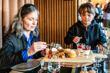 Frau und Junge sitzen an einem Tisch und essen verschiedene Desserts von einem Holzbrett.