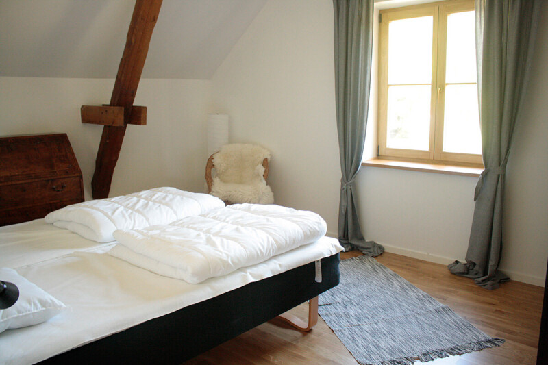 Heller Flur mit Holzboden, weißer Bank mit gemustertem Sitzkissen, offenem Holztür mit Glasfenster und Zugang zu Balkon, an der Wand ein Poster und ein schwarzer Stuhl