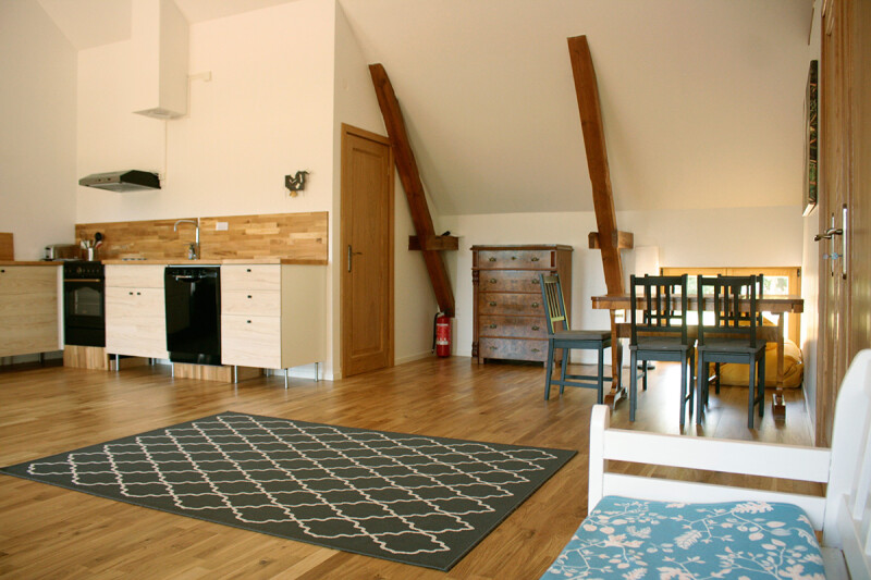 Offene Wohnküche mit Holzboden, weißen Schränken, Holzarbeitsplatte, Esstisch mit Stühlen und sichtbaren Holzbalken unter einer Dachschräge in einer Wohnung auf Öland, Schweden