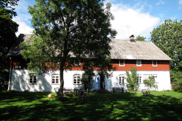 Großes, zweistöckiges Bauernhaus mit weißem Erdgeschoss und rotem Obergeschoss hinter Bäumen auf einer grünen Wiese in Schweden