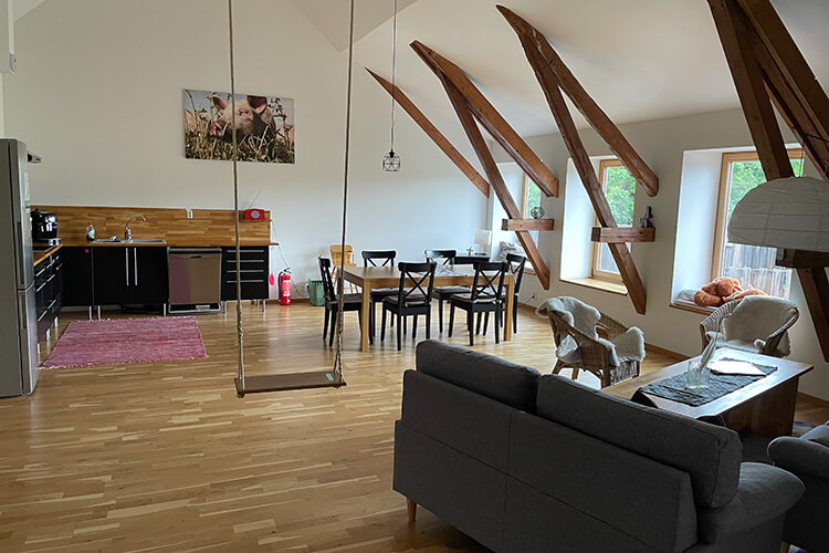 Wohnraum mit Holztreppe zur Empore, Schreibtisch mit Stuhl, Sofa, zwei offenen Türen zu Schlafzimmern und Wanddekoration mit Spiegel und Poster