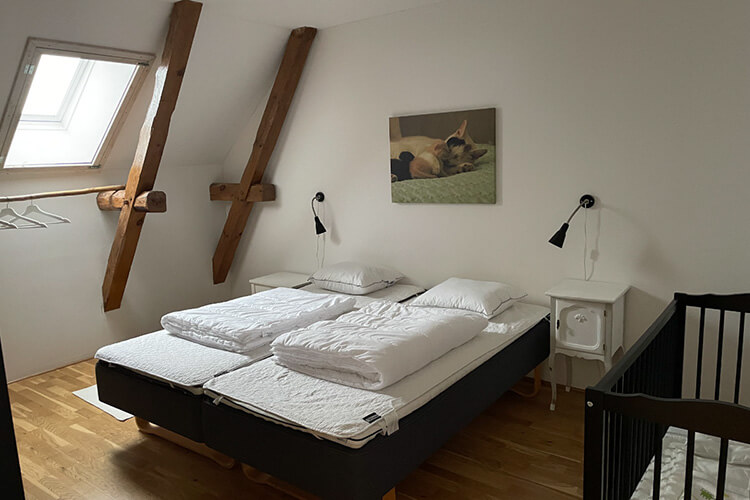 Schlafzimmer im Ferienhaus mit Babybett aus Holz neben dem Doppelbett.