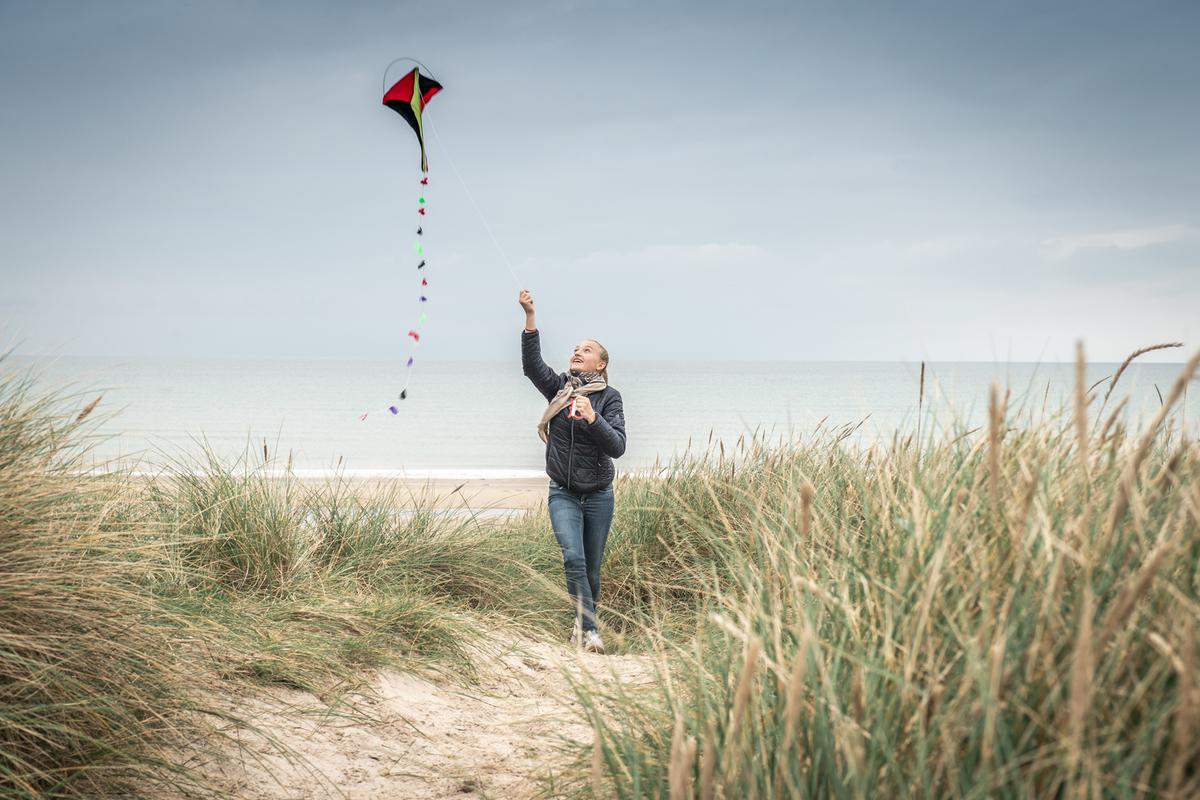 Ein Koch läuft durch die Dünen am Strand mit einem Drachen, den es an der Leine hält.